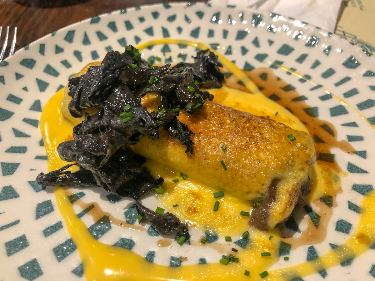 Canelones de rabo de toro servidos con verduras de hoja cocidas y salsa amarilla.