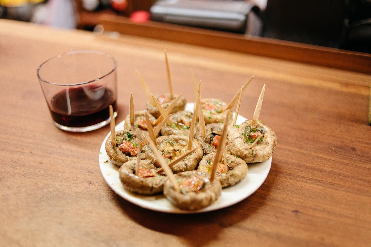 Plato de setas a la plancha con chorizo junto a una copa de vino tinto.