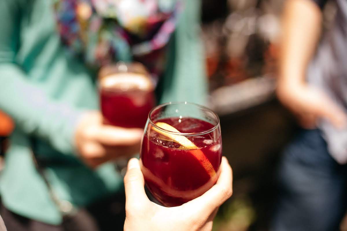 Mano de la persona sosteniendo una copa de un cóctel de vino tinto adornado con una rodaja de limón.