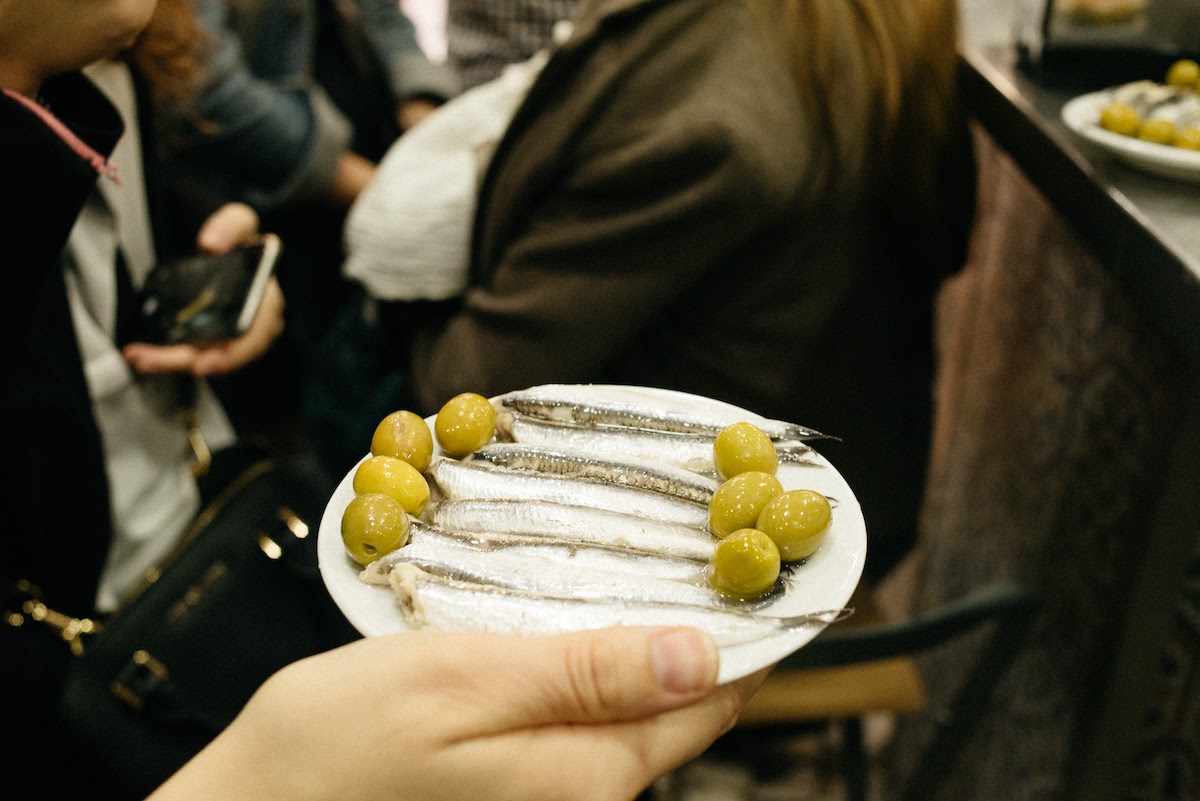 Mano de la persona sosteniendo un plato de anchoas y aceitunas verdes.