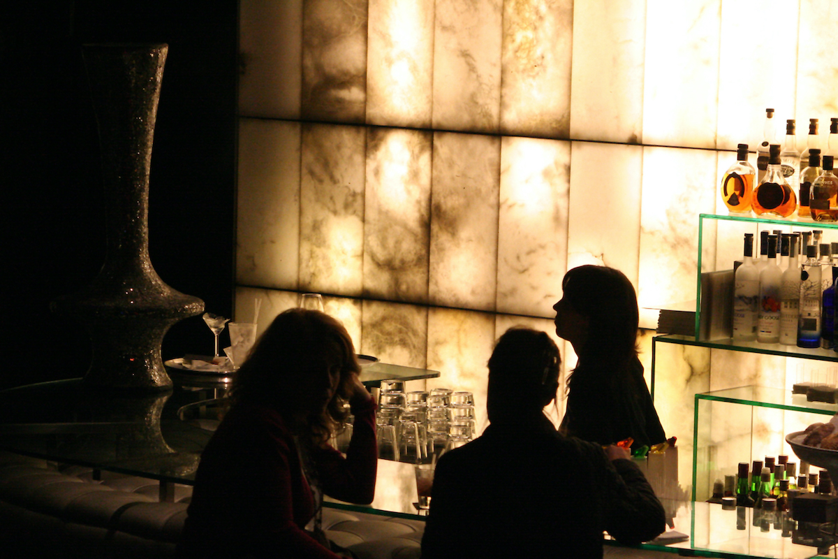 Imagen retroiluminada de personas sentadas en un bar de cócteles bien iluminado.