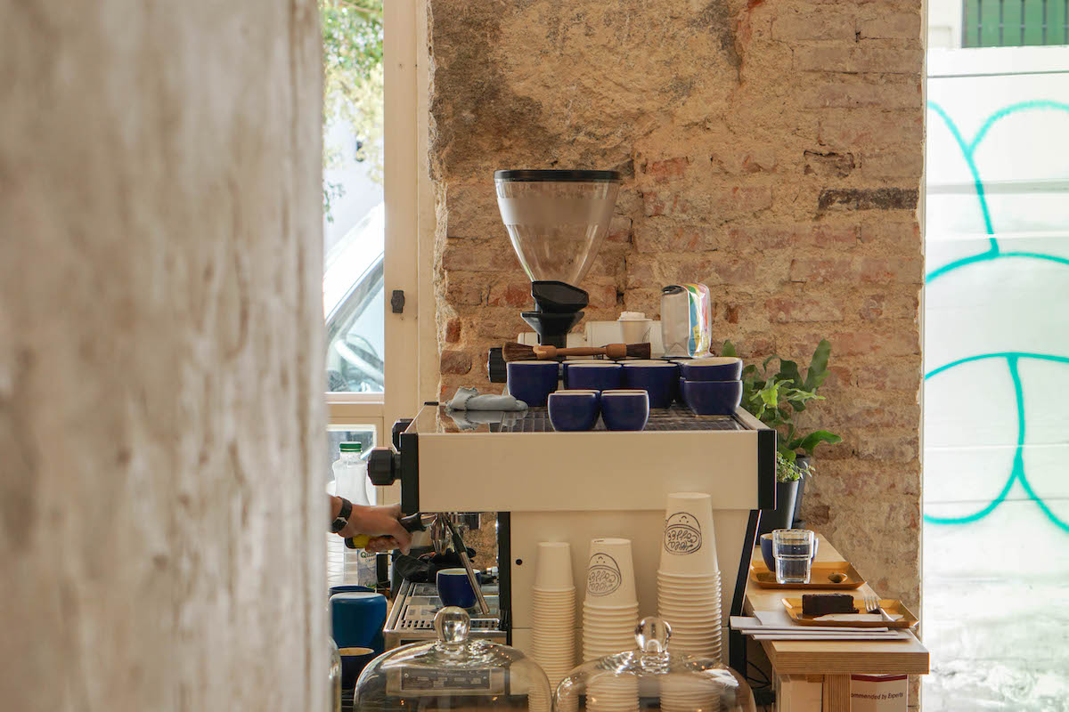 Mostrador en una cafetería con una máquina de espresso, vasos de papel blanco y tazas azules.