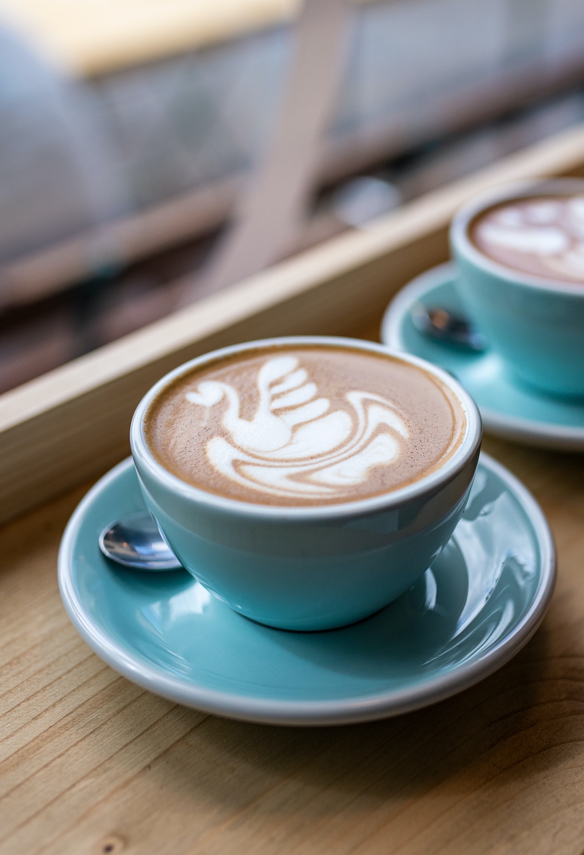 Latte con leche dibujada en forma de cisne servido en una taza verde azulado.