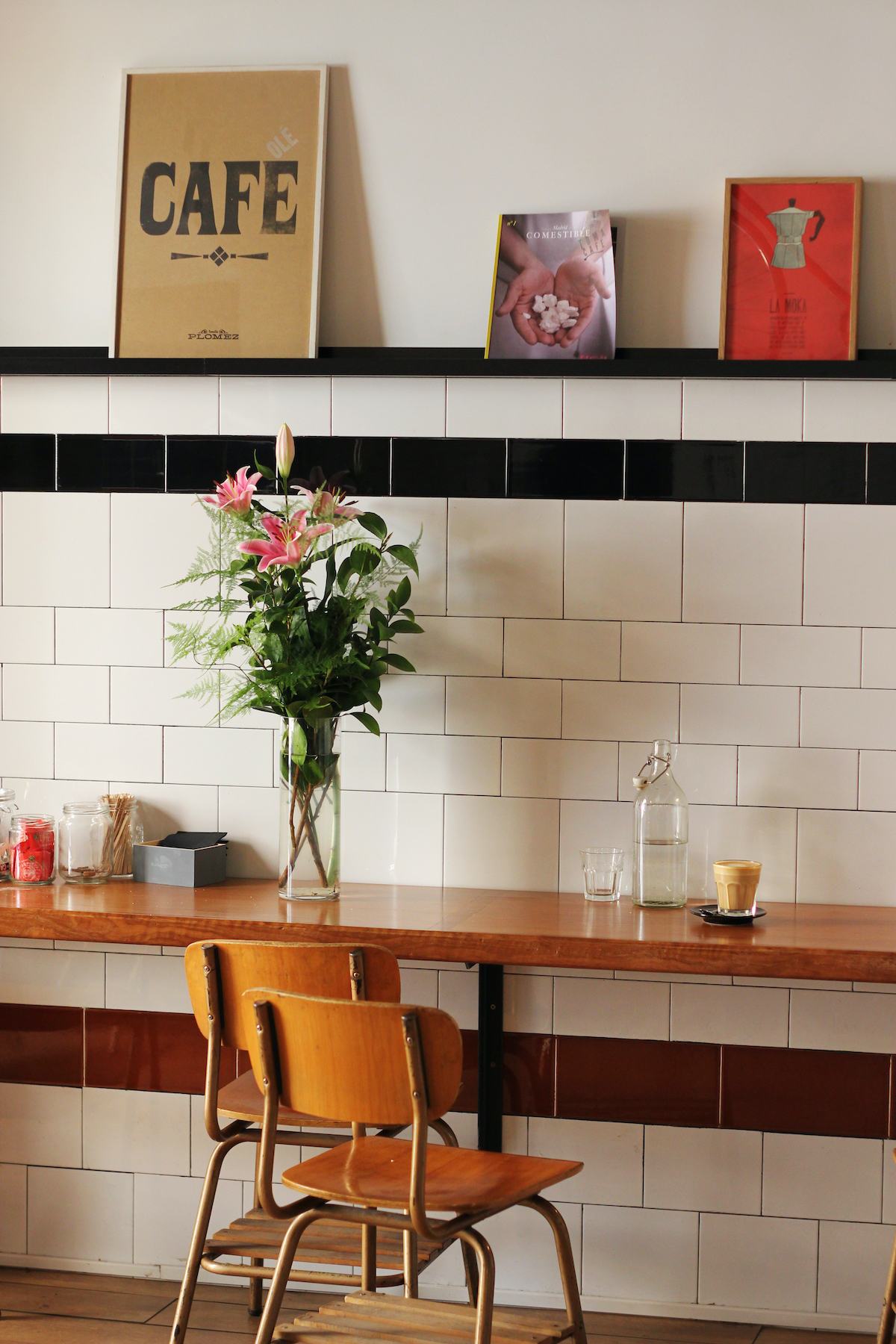 Mostrador de madera contra una pared con dos sillas de madera en el frente y una taza de café encima, con una decoración con temática de café en la pared de arriba.