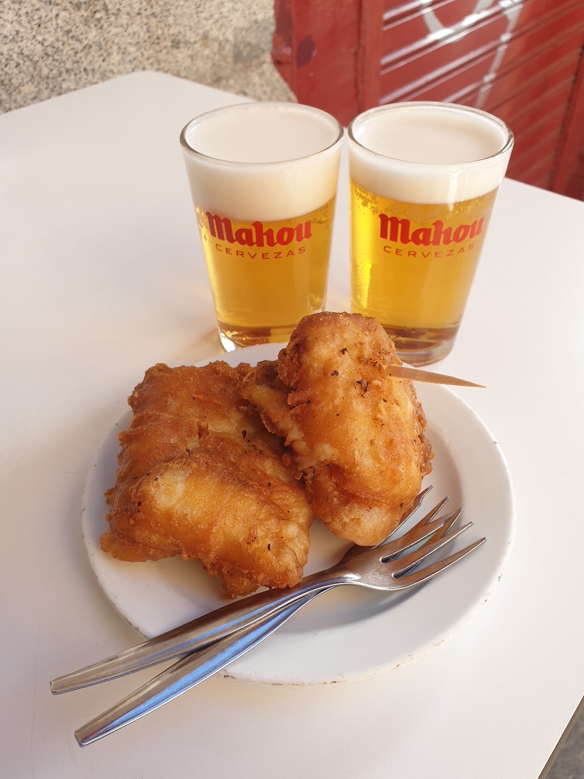 Trozos de bacalao frito en un plato blanco delante de dos vasitos de cerveza de Casa Revuelta de Madrid