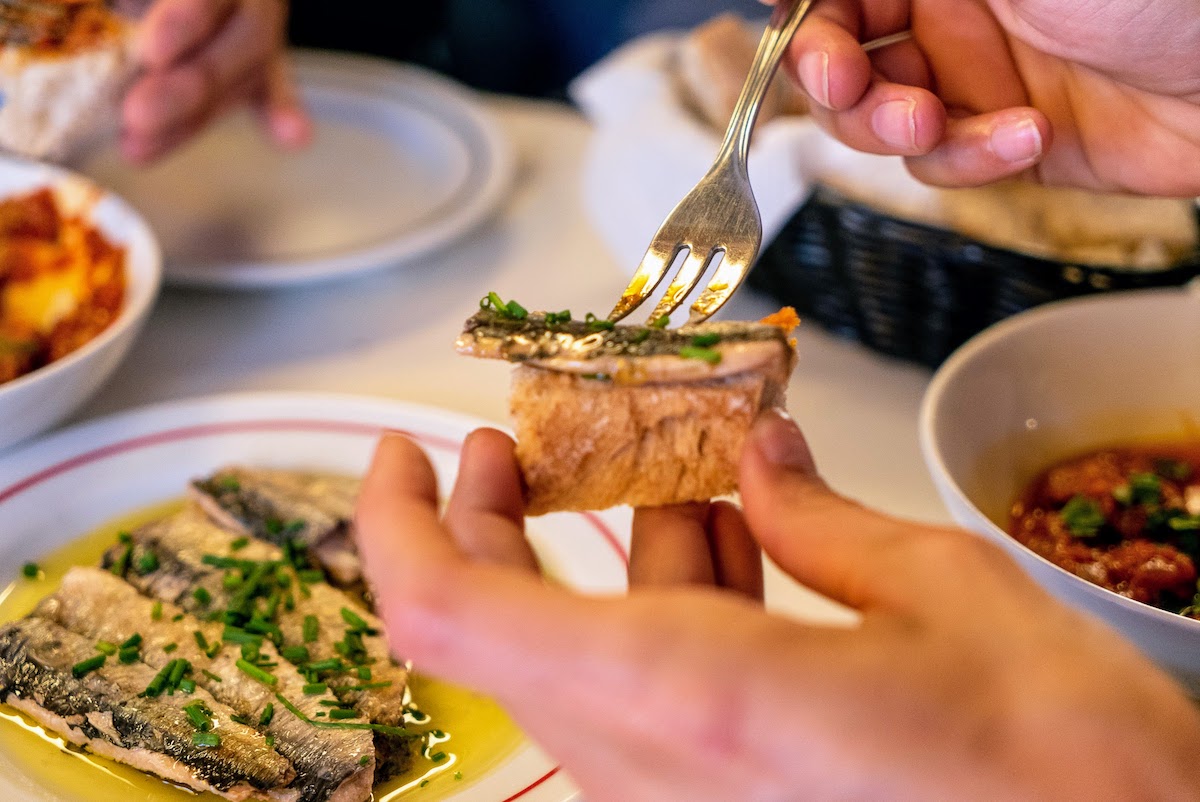 Primer plano de una persona poniendo un trocito de pescado encima de un trozo de pan con un tenedor