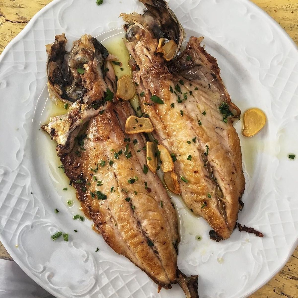Dos trozos de pescado cocido con guarnición de hierbas en un plato blanco.