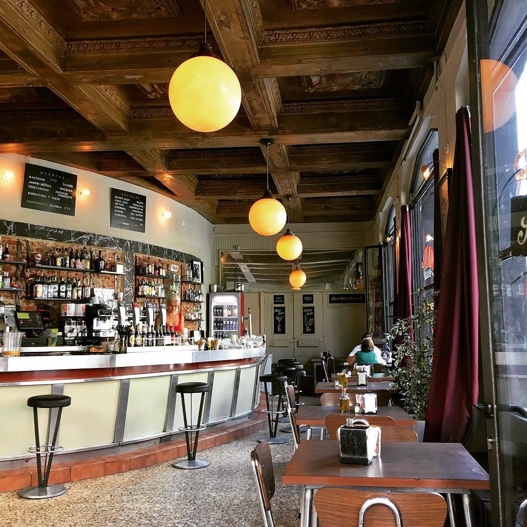 Interior de un café-bar anticuado con lámparas globo en el techo y paneles de madera.