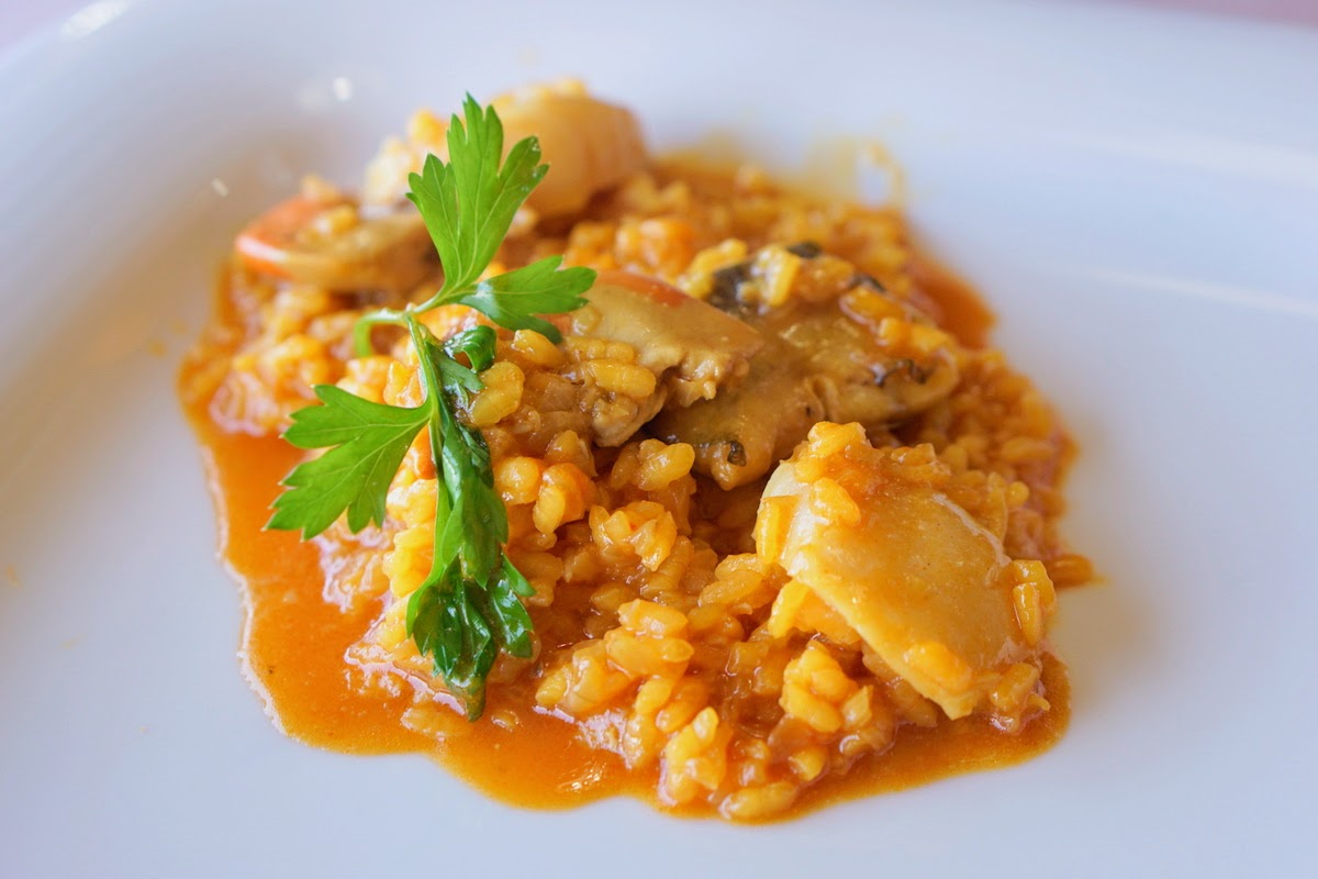 Arroz de marisco en caldo pardo anaranjado con guarnición de hierbas frescas.