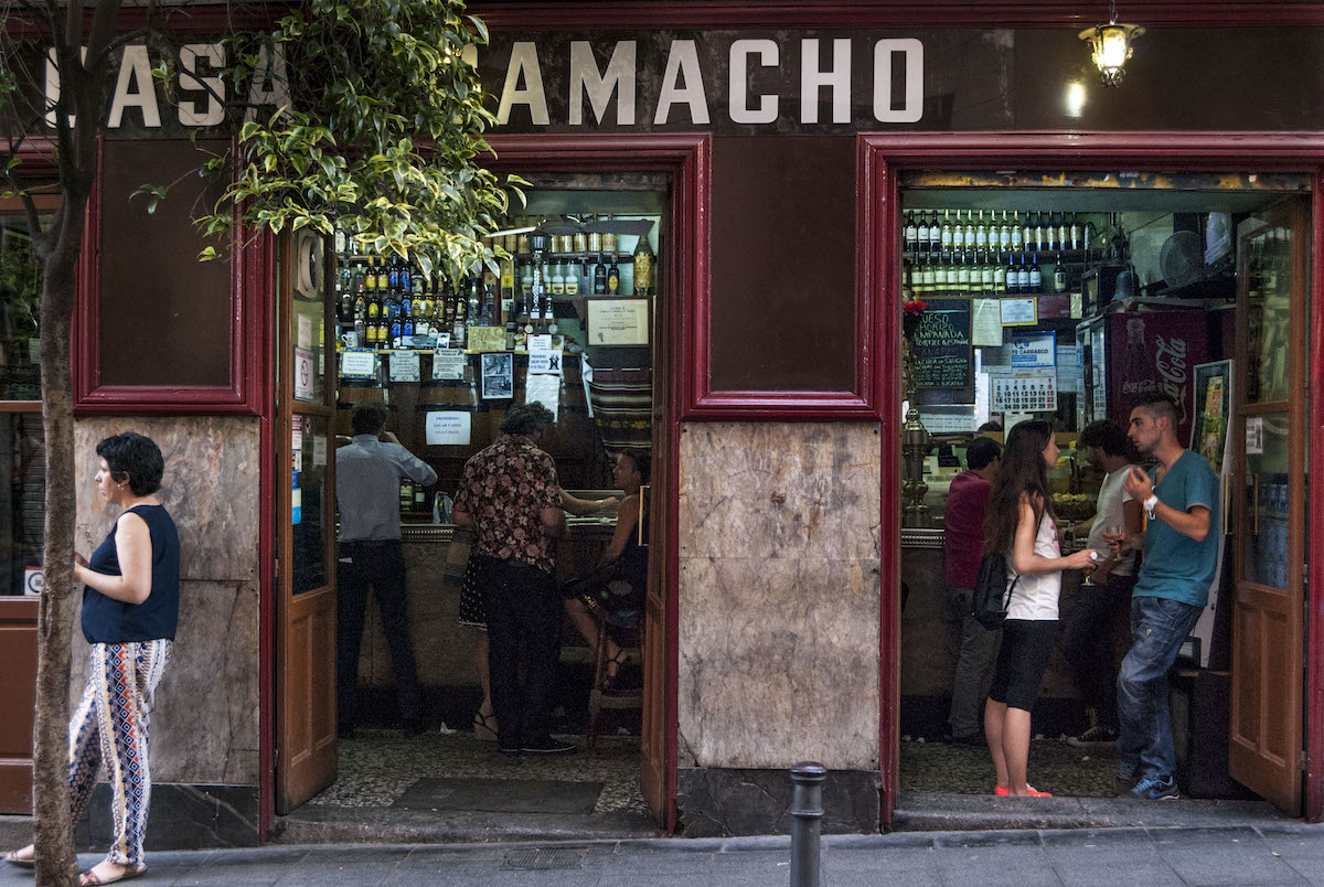 Gente de pie en la puerta de un restaurante rojo de Malasaña en el que se lee Casa Camacho.