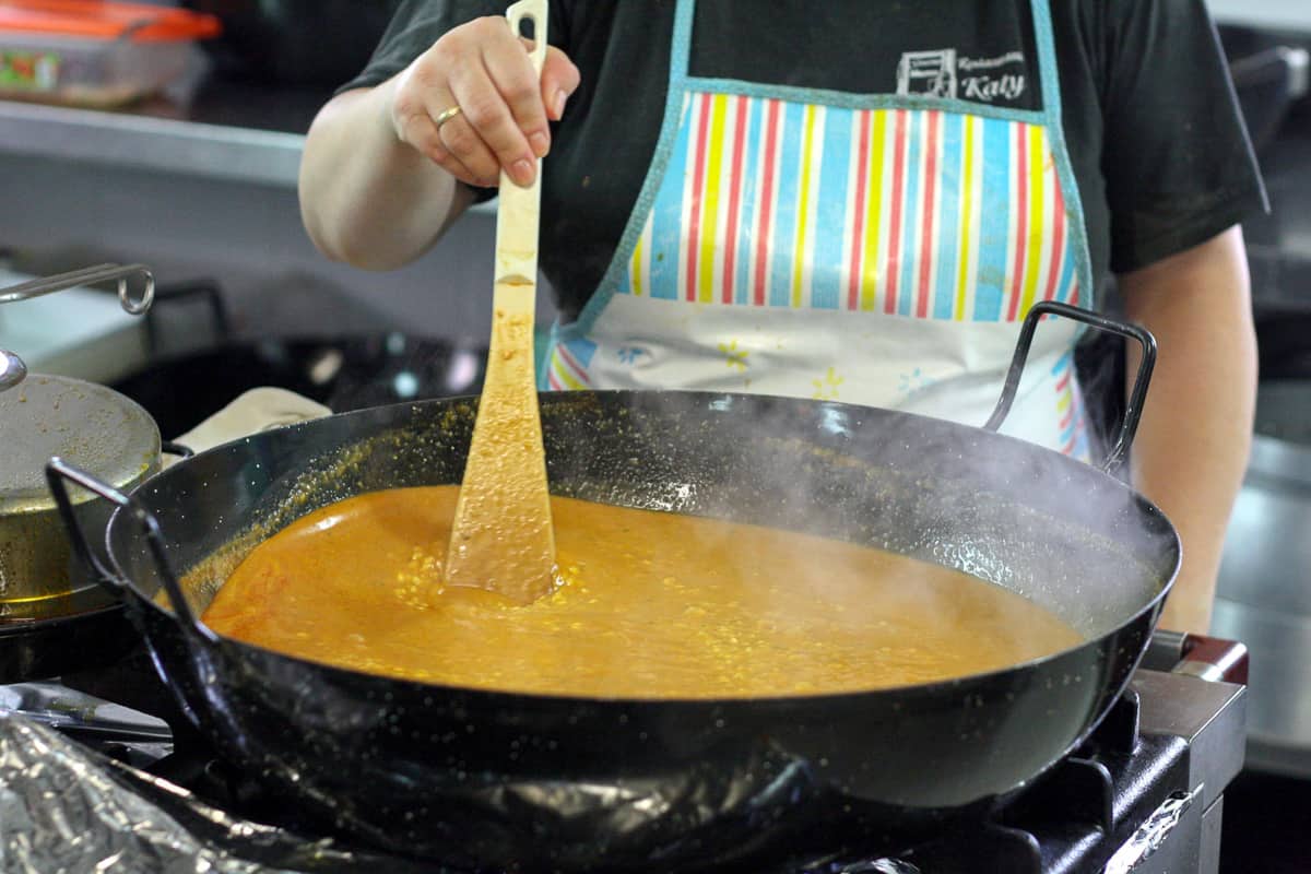 Una persona remueve un plato de arroz caldoso en una gran olla negra