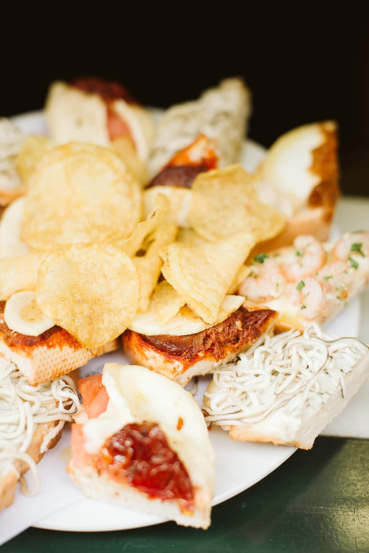 Plato de pequeños bocadillos abiertos con varios ingredientes, con un montón de patatas fritas en el centro.