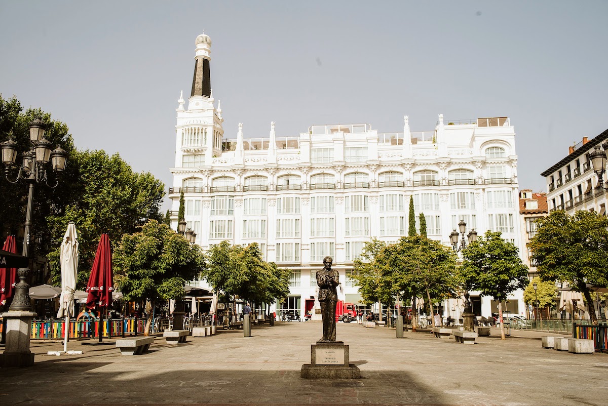 Plaza urbana con una estatua de un hombre en primer plano y un gran hotel blanco al fondo.