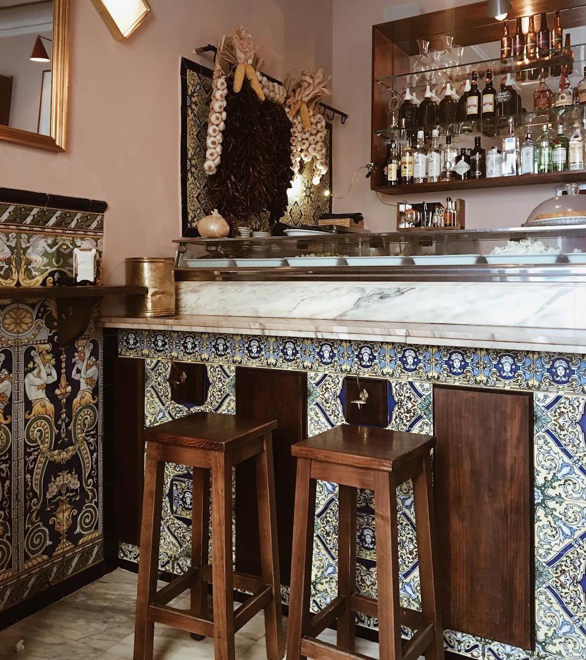 Barra de mármol con azulejos de colores y dos taburetes de madera delante.